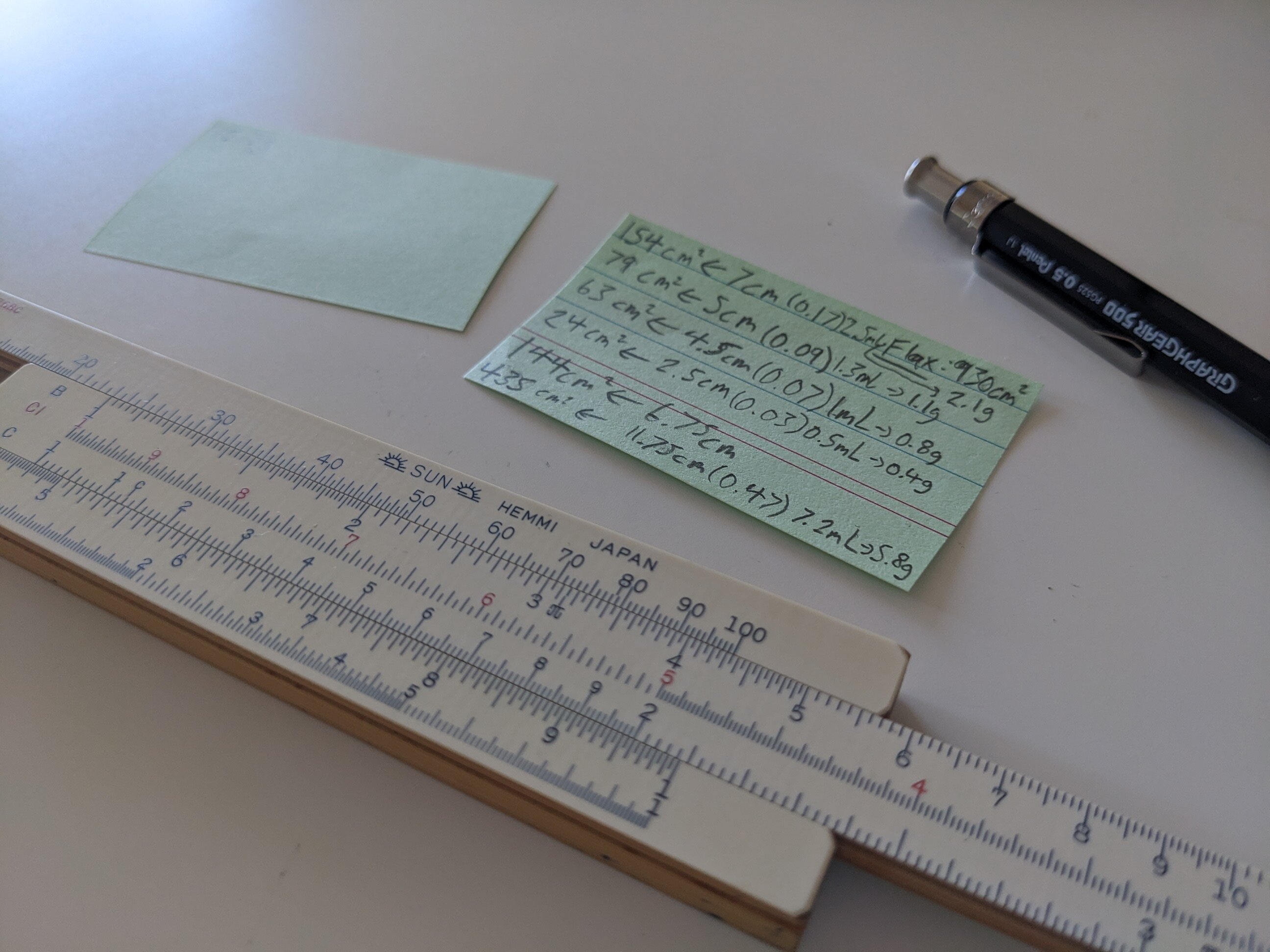 A slip of paper with calculations written on it, and a wooden slide rule.