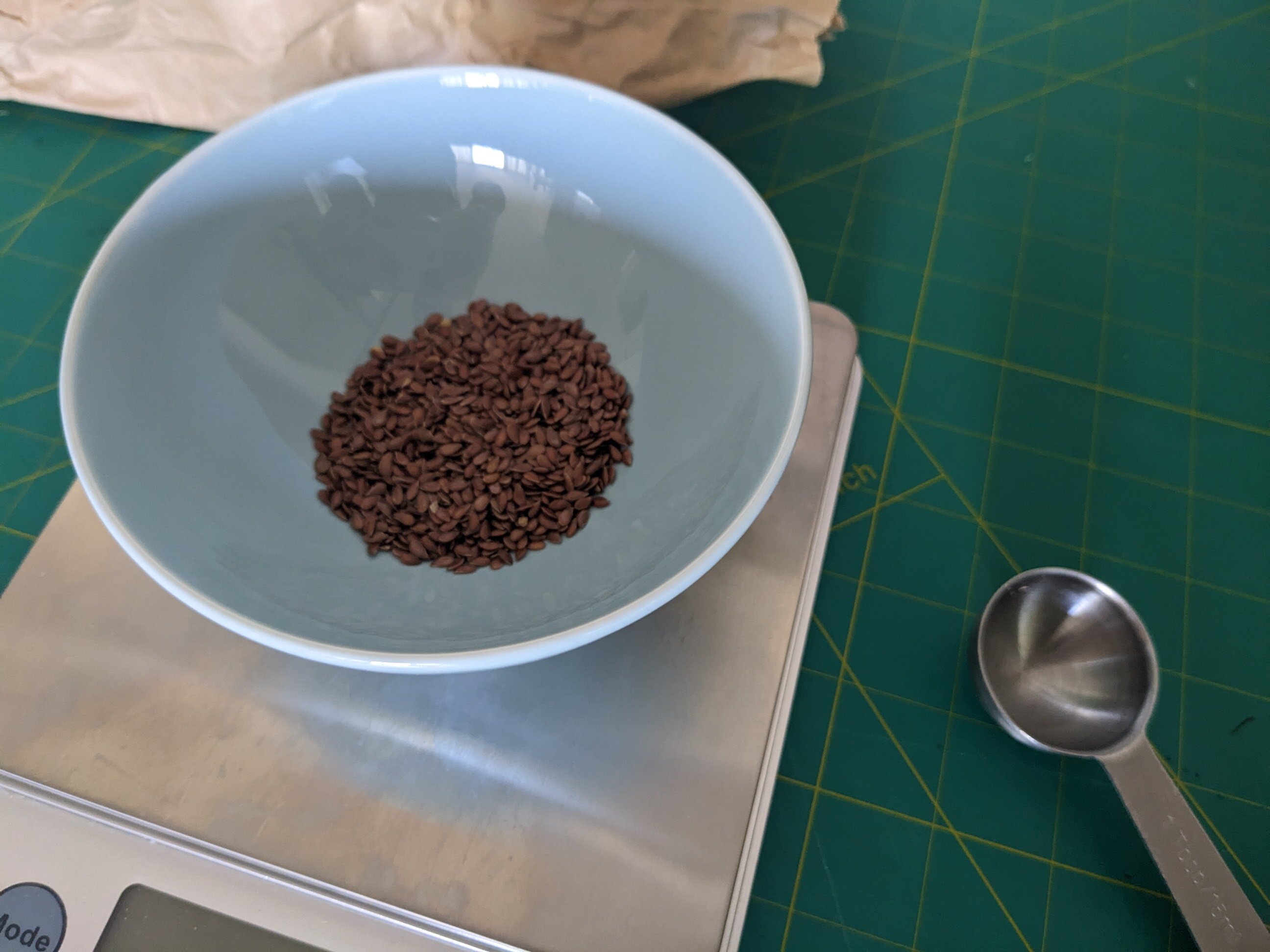 A tablespoon of brown flax seeds, in a light blue dish, on a kitchen scale.