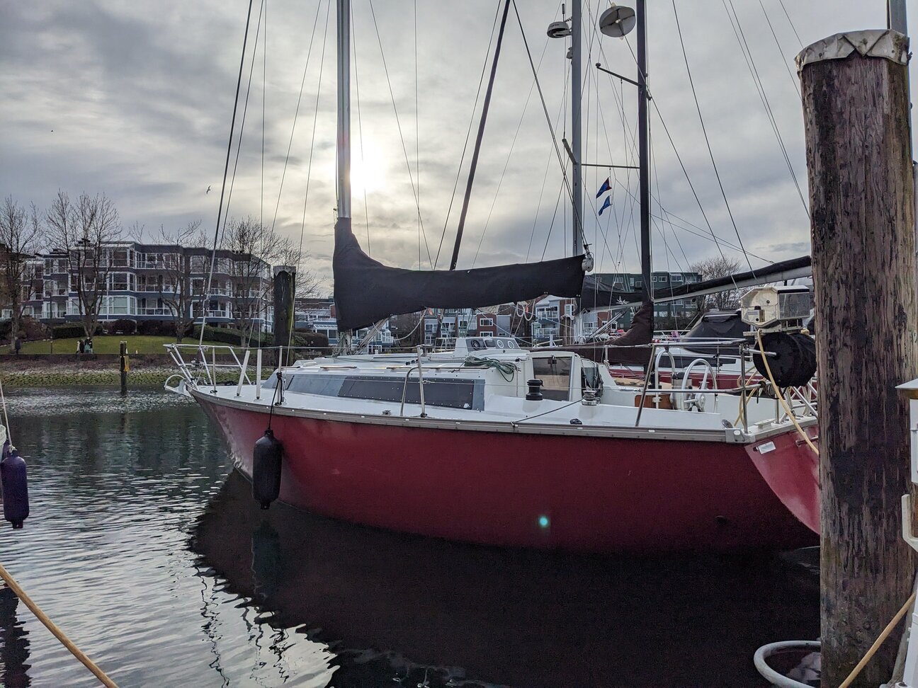 A docked sailboat with a red hull and white deck. Its mainsail is packed away in a cover on the boom.